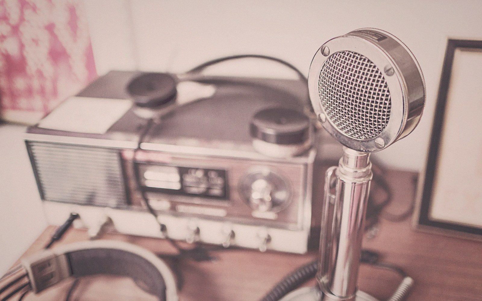 A round microphone stands beside a vintage radio with knobs and headphones on a desk
