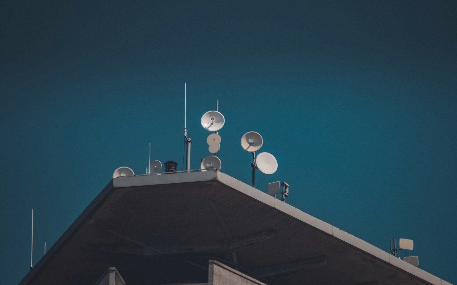 Satellite dishes and antennas mounted on a rooftop against a dark blue sky