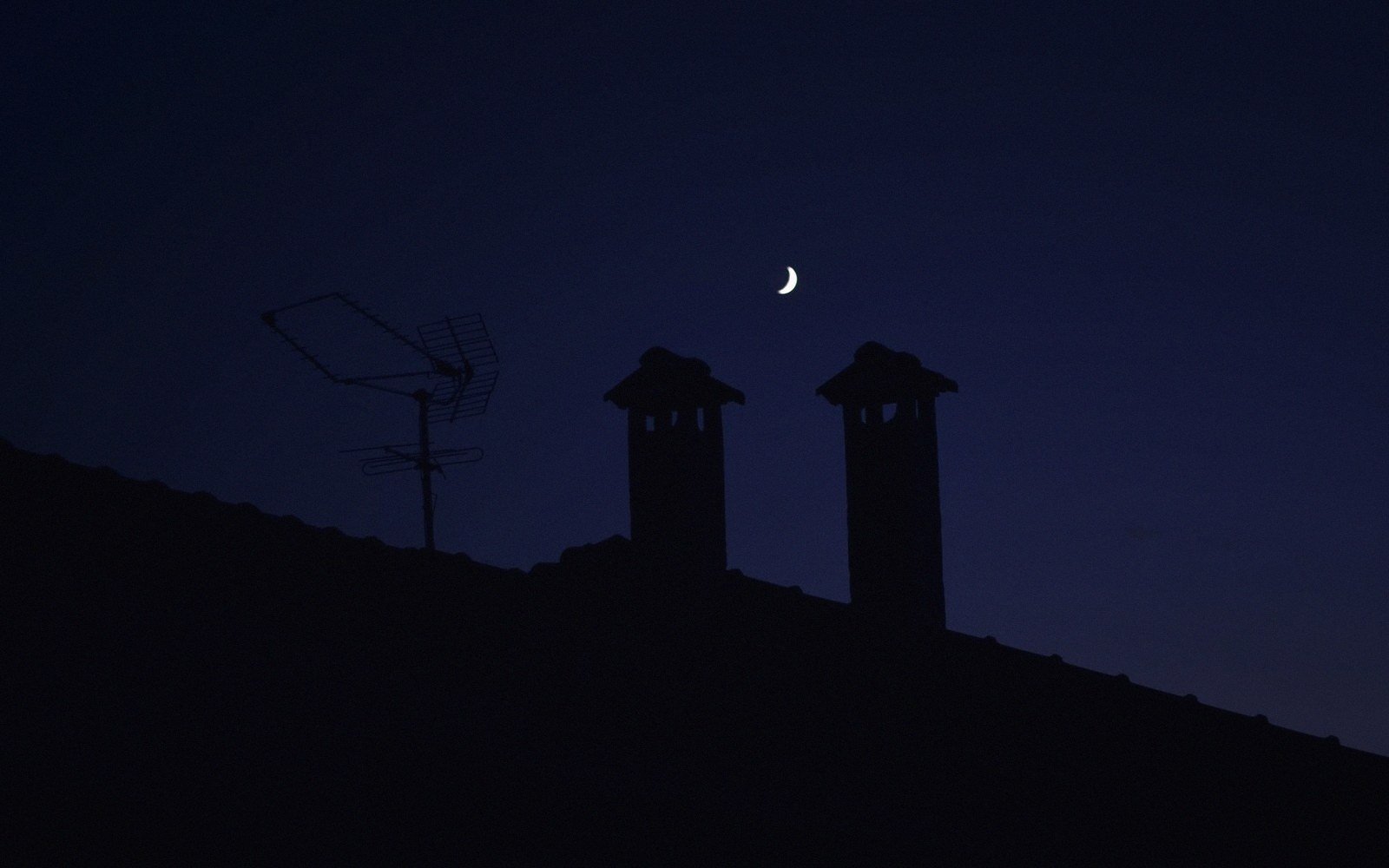 Crescent moon glowing above rooftop chimneys and a TV antenna at dusk
