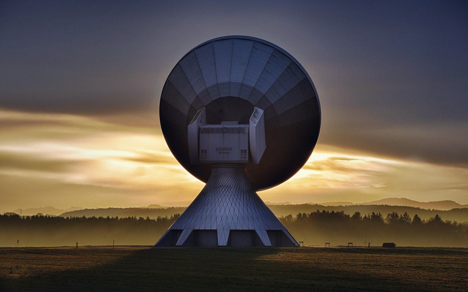 Large satellite dish antenna silhouetted against a glowing sunset sky