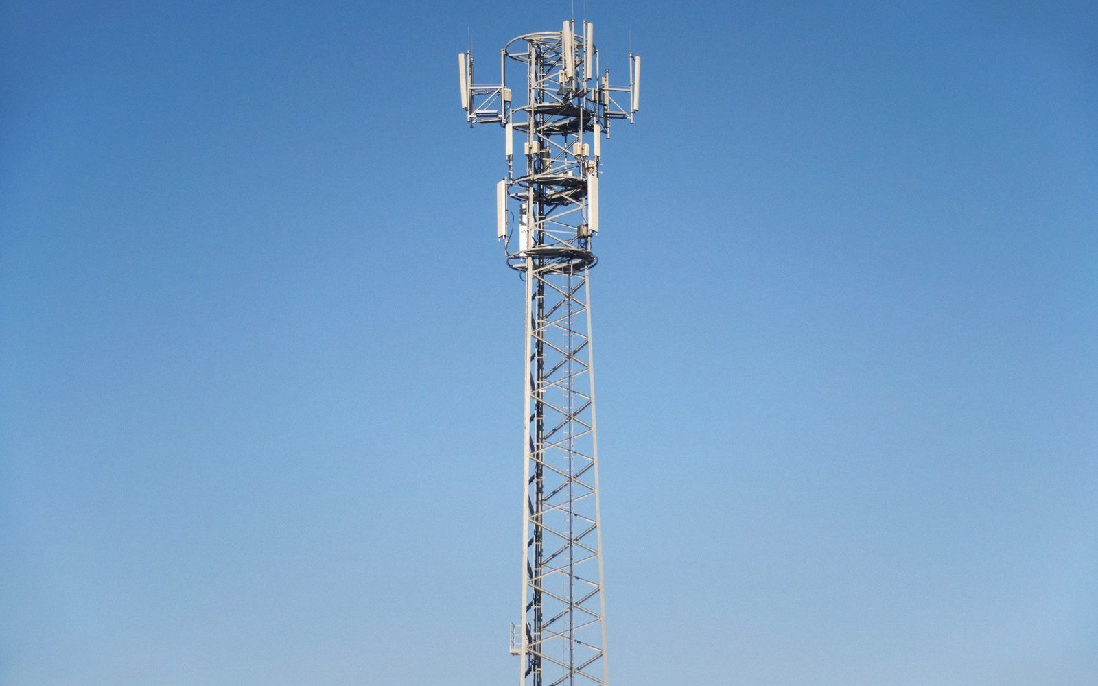Tall lattice cell tower with mounted antennas rising against a clear blue sky